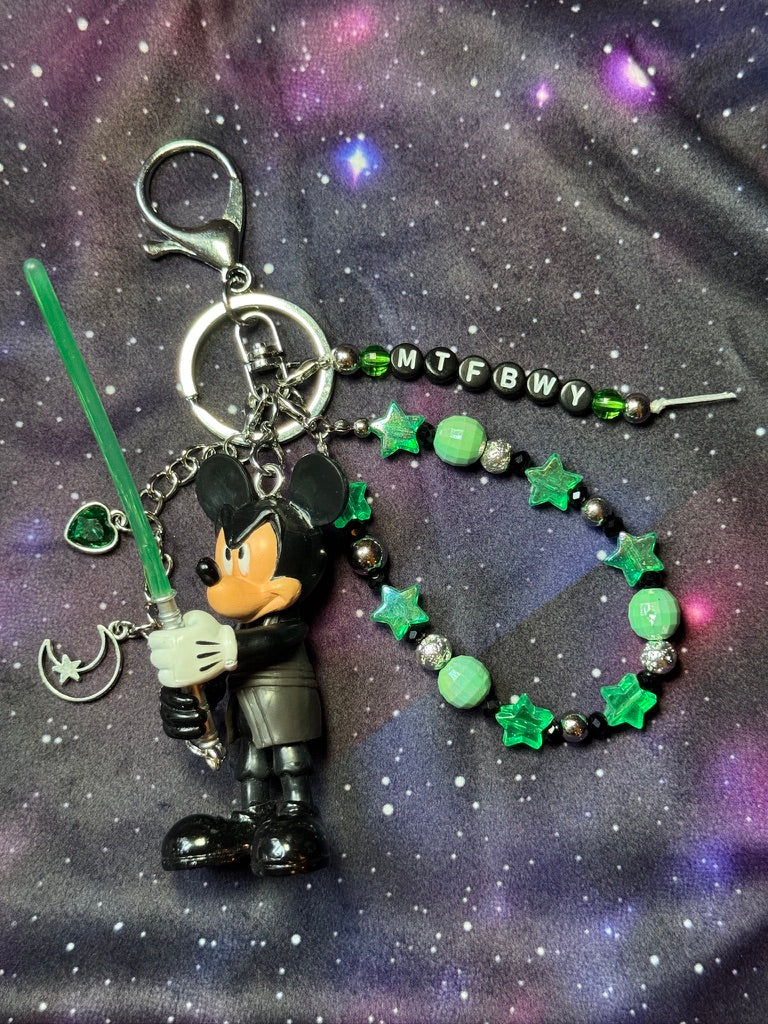 Mickey Mouse figure dressed in black outfit styled like Luke Skywalker from Return of the Jedi. Figure is attached to a silver keychain with green, silver and black charms and beads. MTFBWY letter charm. 