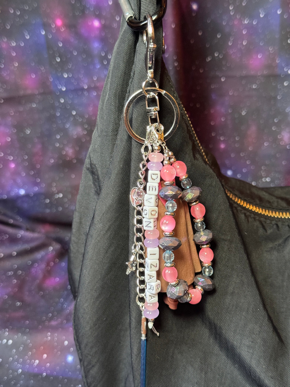 Devon Izara character from Star Wars action figure that has been turned into a bag charm/keychain. Attached to a silver keychain with coordinating beads and charms in a pink, blue and silver color scheme. Bag charm is attached to a black purse set against a purple background. 