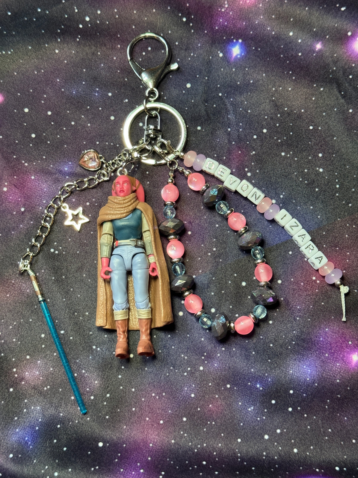 Devon Izara character from Star Wars action figure that has been turned into a bag charm/keychain. Attached to a silver keychain with coordinating beads and charms in a pink, blue and silver color scheme. Bag charm is set against a purple background. 