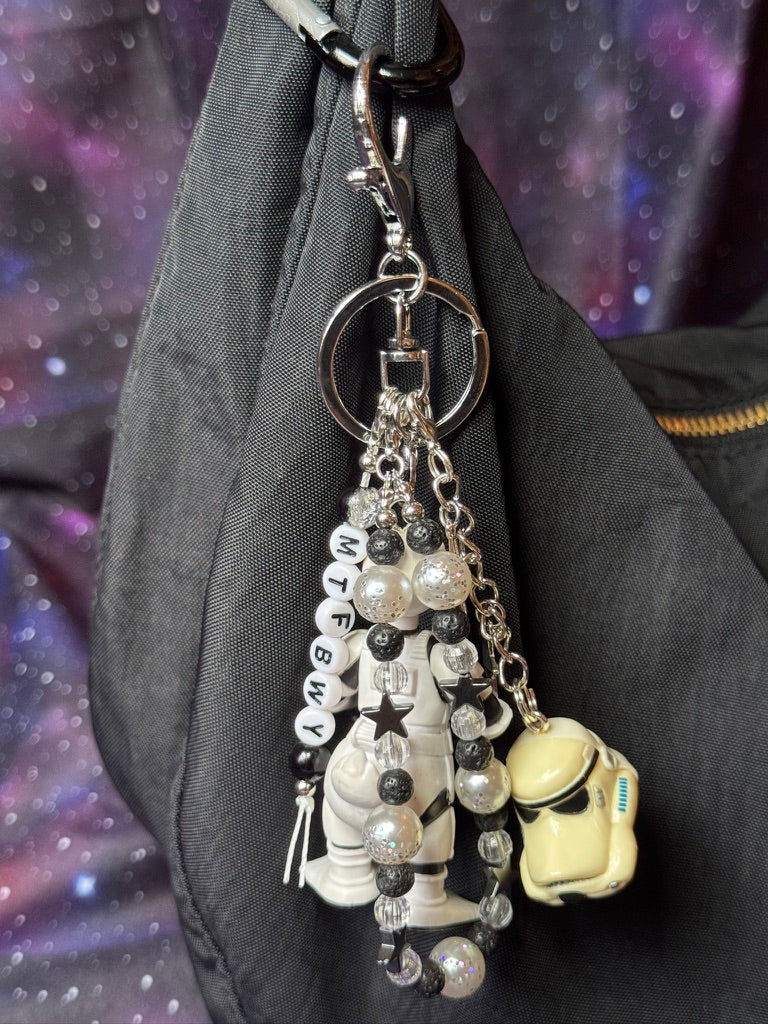 Donald Duck styled as a Stormtrooper from Star Wars figure. Attached to a silver keychain with coordinating beads in a black, silver and white color scheme. Figure is attached to a black purse set against a purple background. 