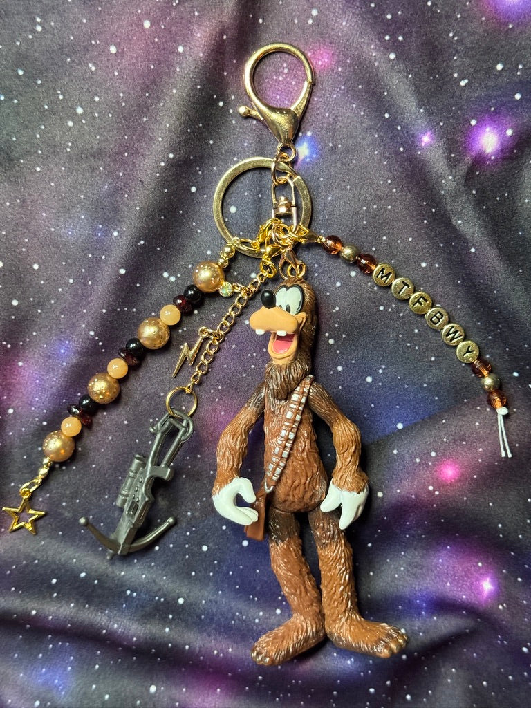 Goofy styled as Chewbacca from Star Wars figure. Attached to a gold keychain with coordinating beads in a brown gold and black color scheme. Figure is set against a purple background. 