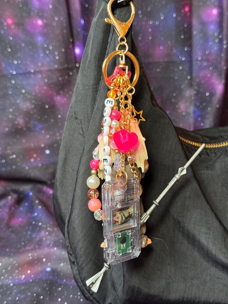 Jar Jar Binks character from Star Wars action figure that has been turned into a bag charm/keychain. Attached to a gold keychain with coordinating beads and charms in a pink, orange and gold color scheme. Figure is attached to a black purse set against a purple background. 