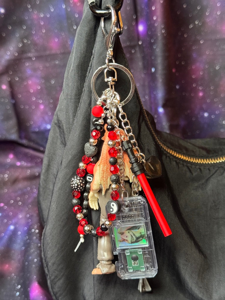 Jar Jar Binks character from Star Wars action figure that has been turned into a bag charm/keychain. Attached to a silver keychain with coordinating beads and charms in a black, silver and red color scheme. Figure is attached to a black purse set against a purple background. 