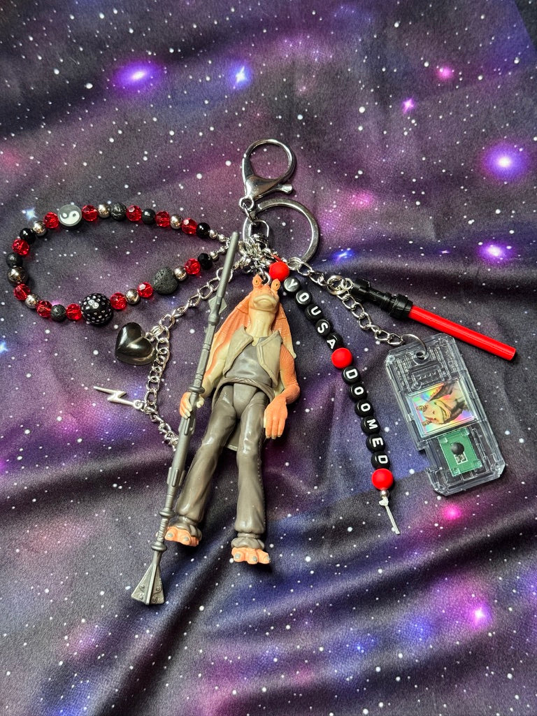 Jar Jar Binks character from Star Wars action figure that has been turned into a bag charm/keychain. Attached to a silver keychain with coordinating beads and charms in a black, silver and red color scheme. Figure is set against a purple background. 