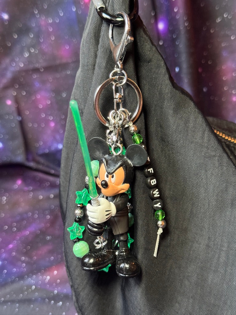 Mickey Mouse figure dressed in black outfit styled like Luke Skywalker from Return of the Jedi. Figure is attached to a silver keychain with green, silver and black charms and beads. MTFBWY letter charm. 